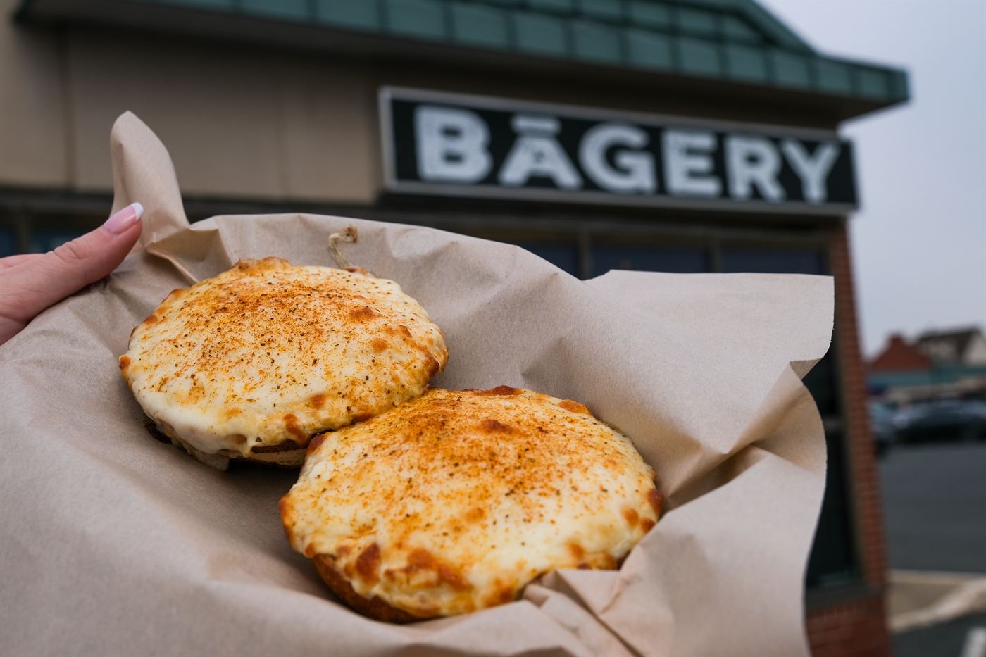 Fresh bagels held up in front of the shop sign