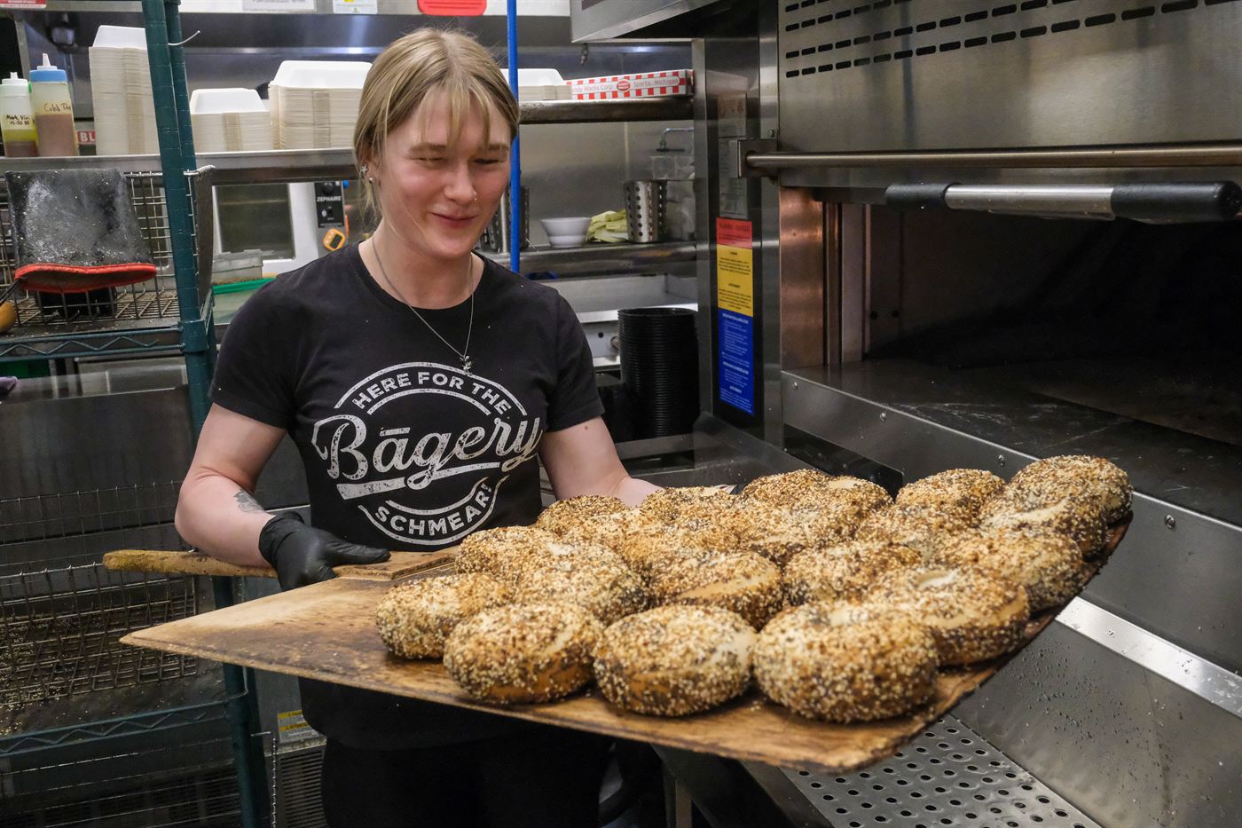 Smiling baker carrying a peel of fresh everything bagels